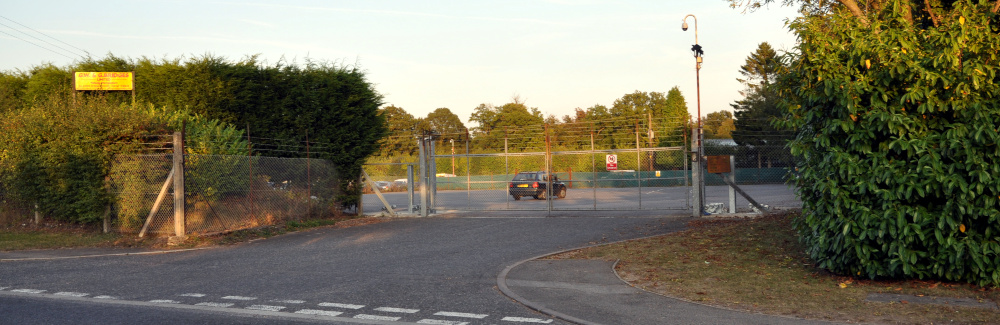 A wide entrance leading to a large empty car park, with trees to the rear and sides