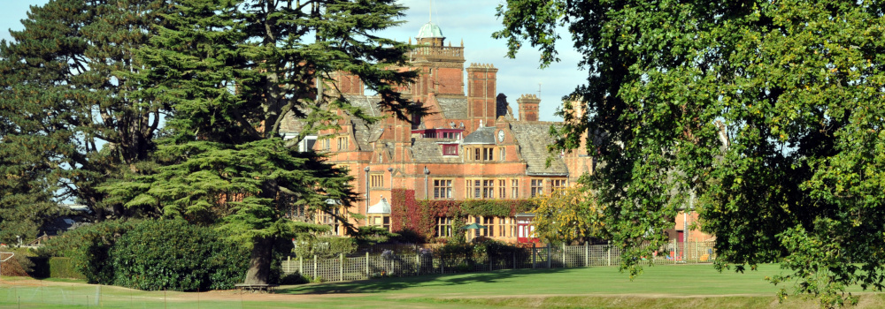 An elaborate red-brick building with lawns at the front and trees at the sides