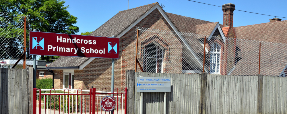 Part of a single-storey building with a fence in front and a sign reading: Handcross Primary School