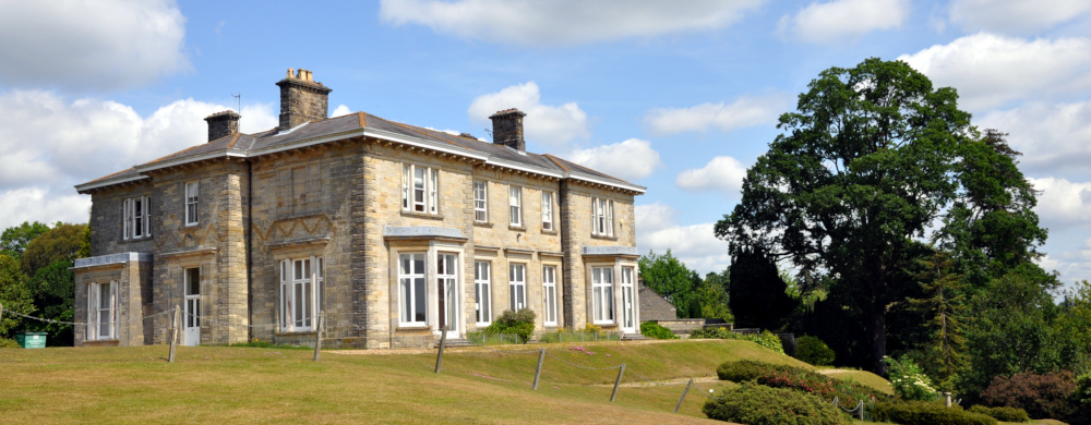 A large, two-storey country house in pale brick, with a lawn in front and trees to the right