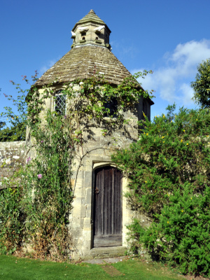 A small stone tower with plants growing on its sides and birds perched on its roof