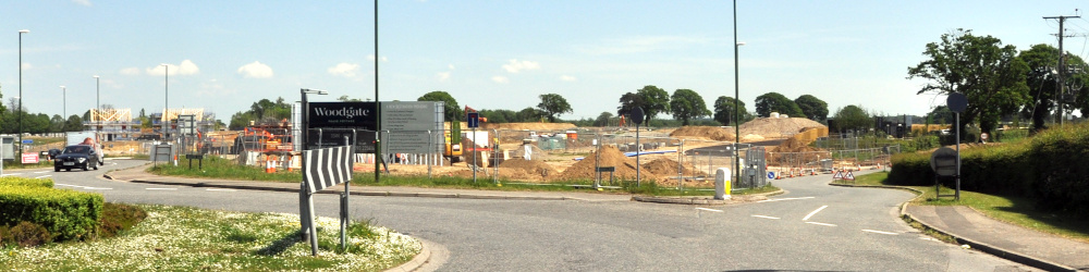 A large building site with a road in the foreground and trees in the background